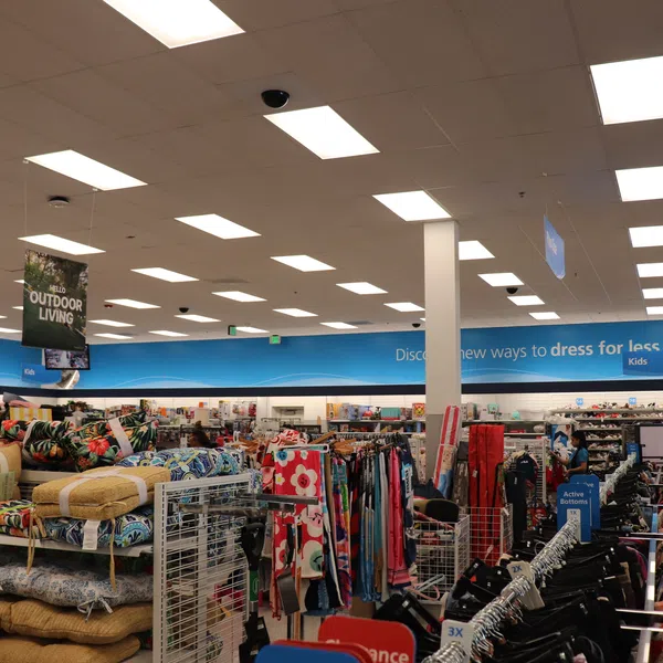 Interior view of a retail store showing clothing racks and colorful cushions under bright ceiling lights.
