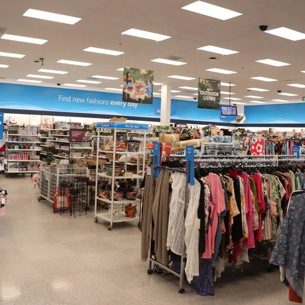 Interior of a brightly lit store with clothing racks and signage for fashion and outdoor living sections.