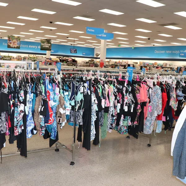 Clothing racks filled with women's swimwear and jackets in a bright retail store with blue signage overhead.