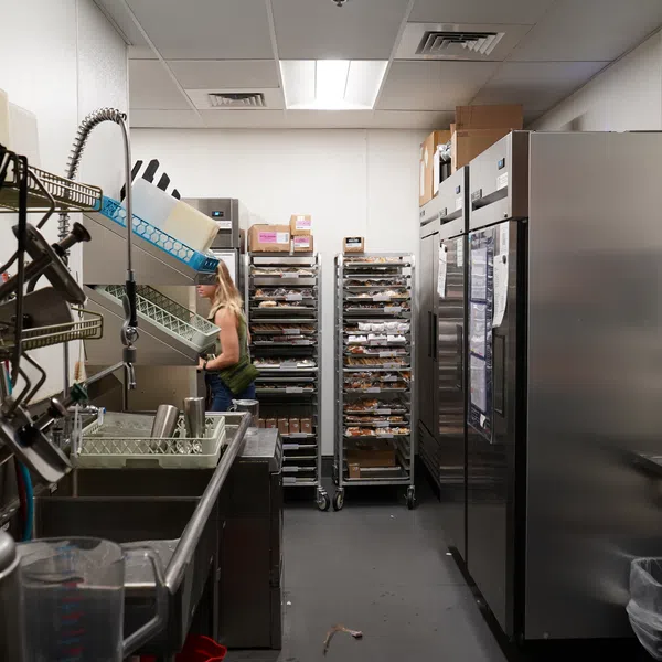 Commercial kitchen with industrial dishwasher, storage racks, and a woman loading dishes in a busy environment