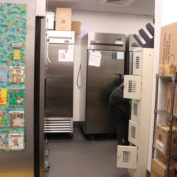 Storage room with refrigerators, shelving filled with cardboard boxes, and a wall decorated with colorful Pokemon-themed artwork.