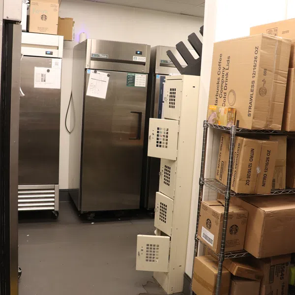 Commercial kitchen storage room with stainless steel refrigerators and shelves full of cardboard boxes.