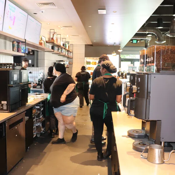 Baristas in black uniforms working behind the counter at a busy coffee shop with coffee machines and menu screens.