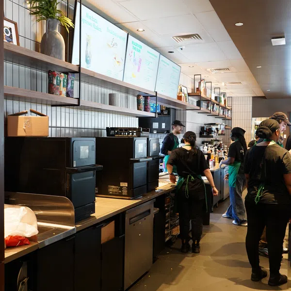 Busy coffee shop counter with staff preparing drinks and digital menu boards overhead