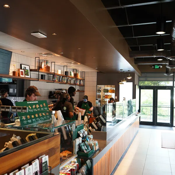 Busy modern coffee shop interior with staff preparing orders and customers seated by large windows.