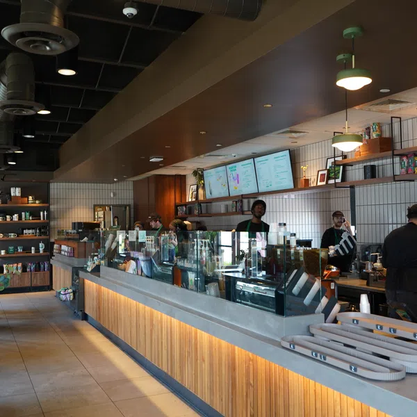 Modern coffee shop interior with wooden counters, baristas behind the counter, and digital menu boards.