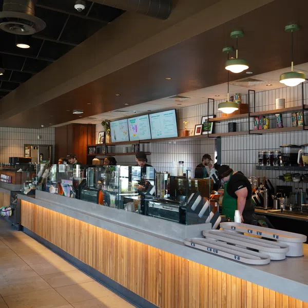 Modern coffee shop interior with baristas behind the counter, menu screens, and warm lighting above wood panels.