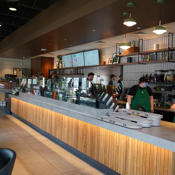 Modern cafe interior with wooden counter, baristas working behind glass display, and menu boards overhead