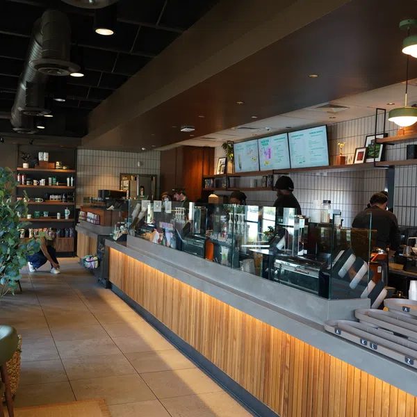 Modern coffee shop interior with wooden counters, baristas preparing drinks, and seating area with plants.