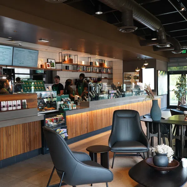 Modern coffee shop interior with wooden counters, black leather chairs, customers, and baristas behind the counter.
