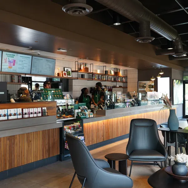 Modern coffee shop interior with wooden counters, digital menu boards, and comfortable seating area with plants.