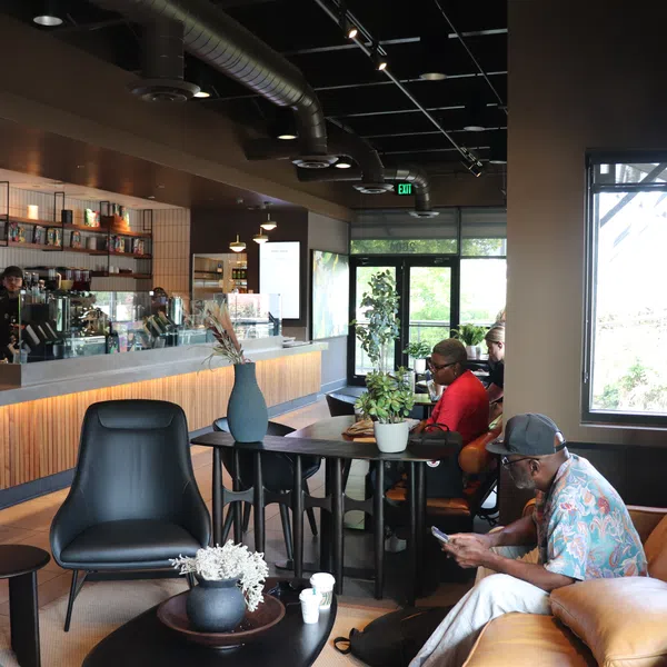 Modern coffee shop interior with customers sitting on leather sofas and bar stools near a wooden counter.