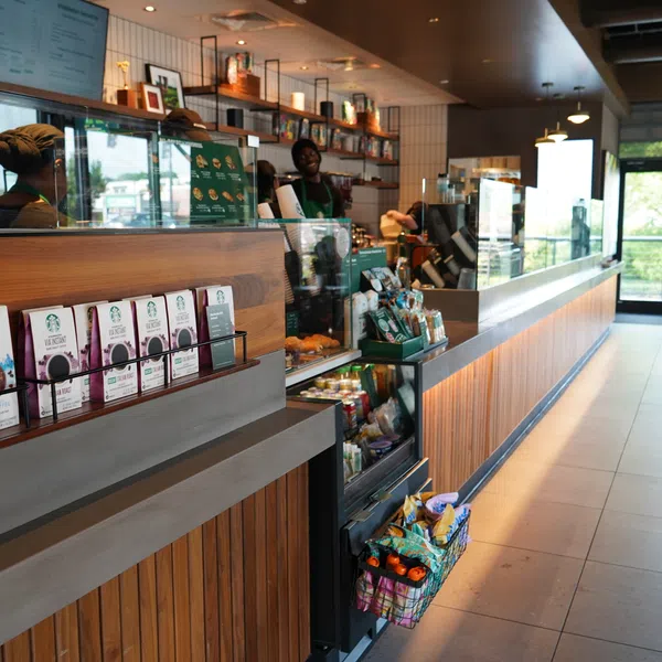 Modern Starbucks café interior with wooden counter, packaged coffee products, and baristas serving customers.