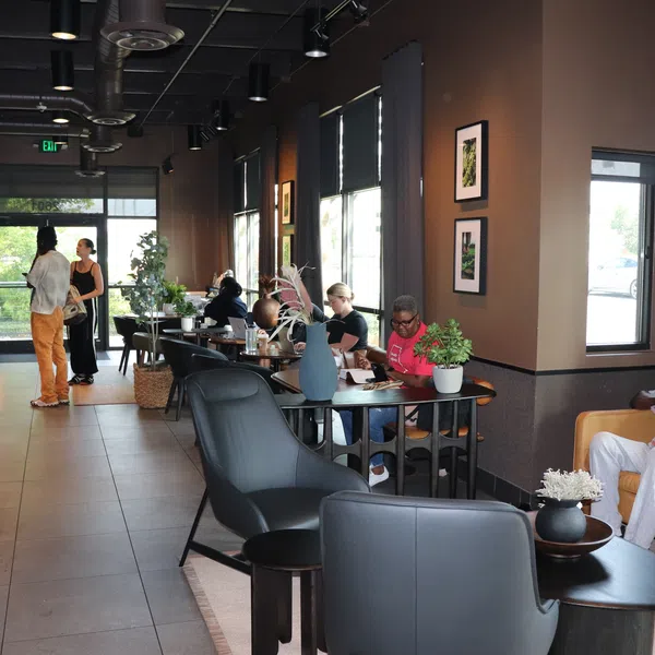 People working and socializing inside a modern, cozy coffee shop with leather chairs and tables.