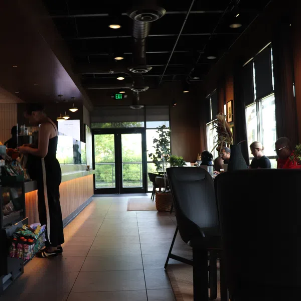 Interior of a modern coffee shop with customers ordering and sitting by windows in cozy seating area.