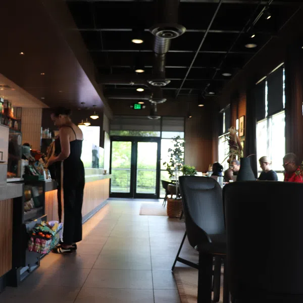 Modern coffee shop interior with customers seated, barista preparing drinks, and natural light from entrance door.