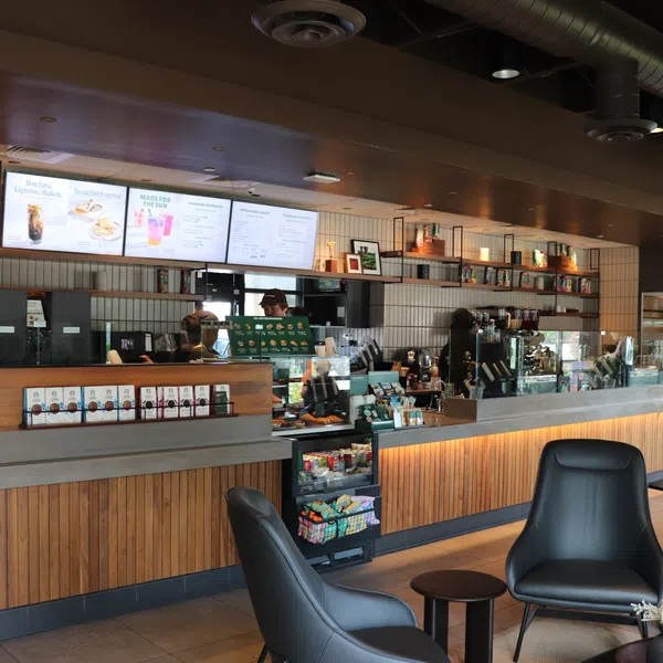 Modern coffee shop interior with wooden counters, black chairs, digital menu screens, and ambient lighting.