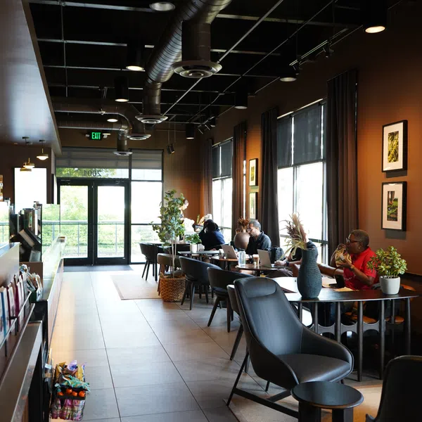 Modern coffee shop interior with people working on laptops, comfortable seating, and warm lighting.