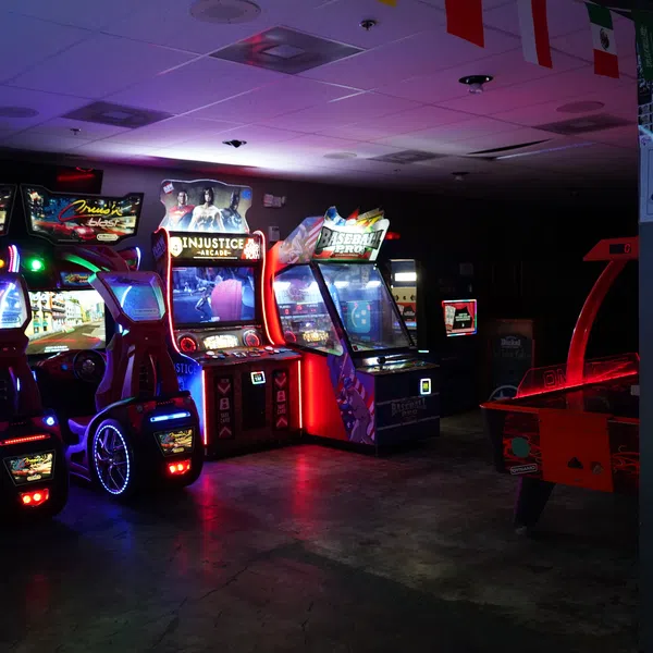 Dimly lit arcade with racing, fighting, and basketball video games illuminated by colorful neon lights.