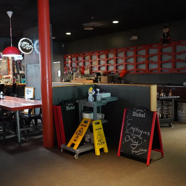 Empty bar area with wooden tables, chairs, cleaning supplies, and an Employees Only sign near kegs and kitchen.