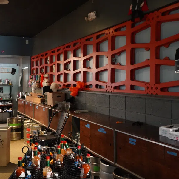 Bar storage area with liquor bottles, kegs, and industrial wood cabinets under red decorative metal wall grid.