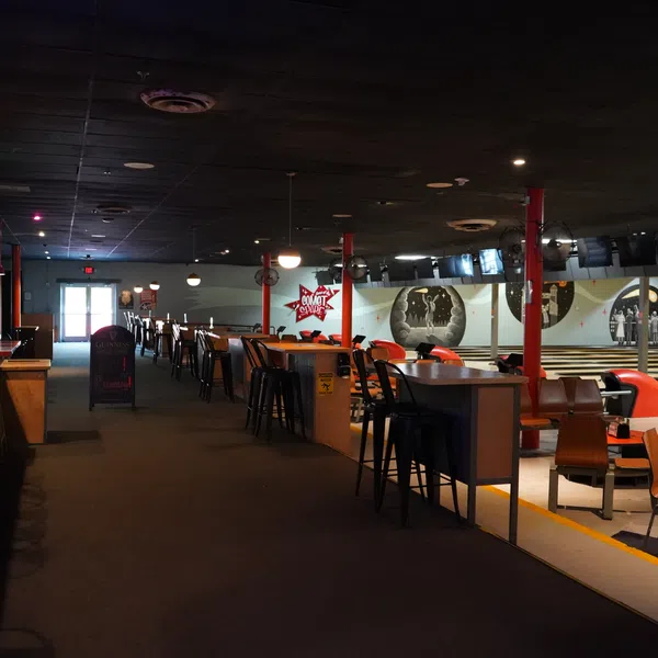 Interior of a bowling alley with lanes, seating areas, bar counter, and wall murals under dim lighting.