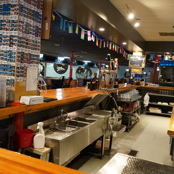 Empty bar interior with wooden countertops, glassware, beer taps, and international flags hanging from the ceiling.