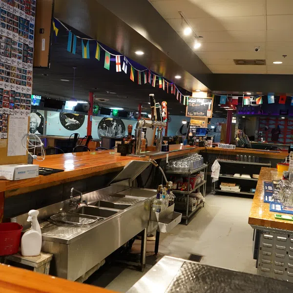 Interior view of a bar with wooden countertops, taps, glassware, and international flags hanging from the ceiling.