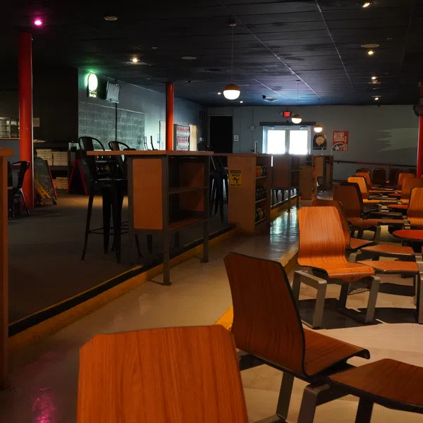Interior view of a dimly lit bowling alley with wooden seating, bowling balls, and lanes in the background.