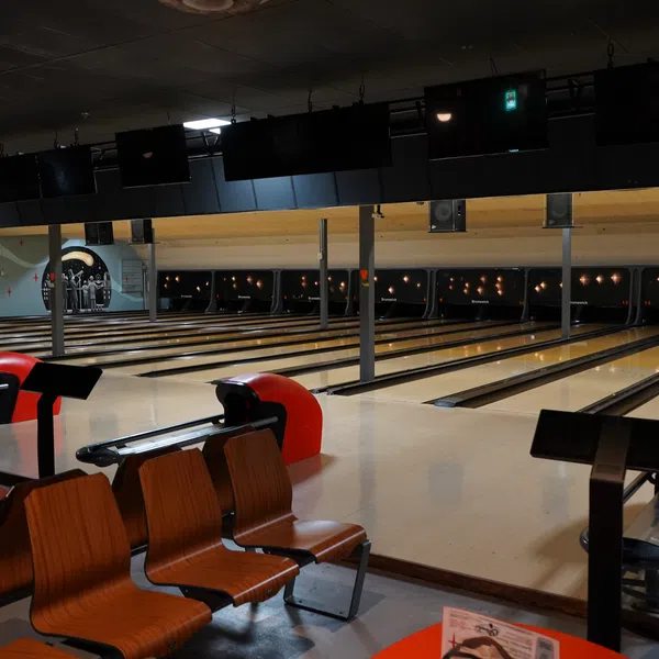Empty bowling alley lanes with wooden seating and ball return machines under dim lighting in an indoor setting