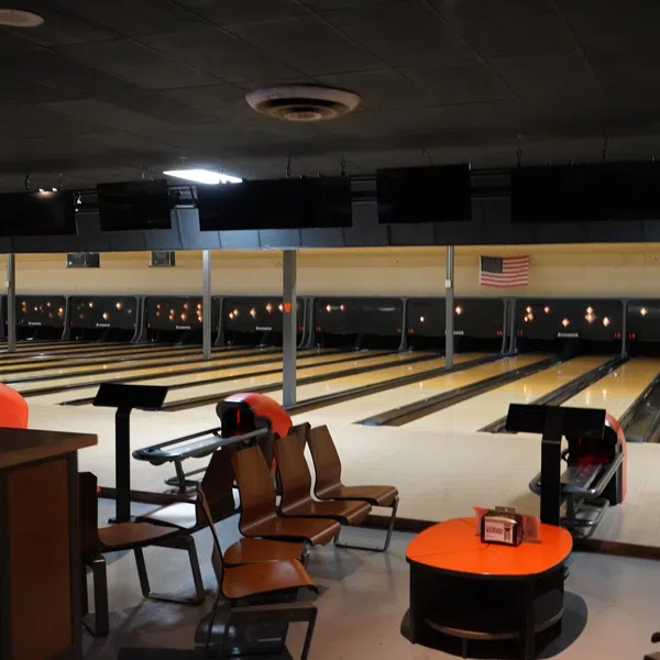 Empty bowling alley with wooden lanes, seating area, and an American flag on the wall under dim lighting.