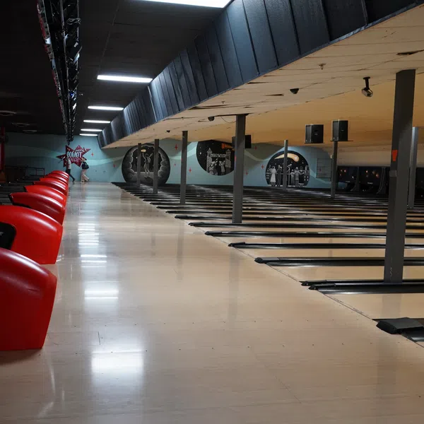 Empty bowling alley lanes with red seating and retro-themed wall murals under ceiling lights.