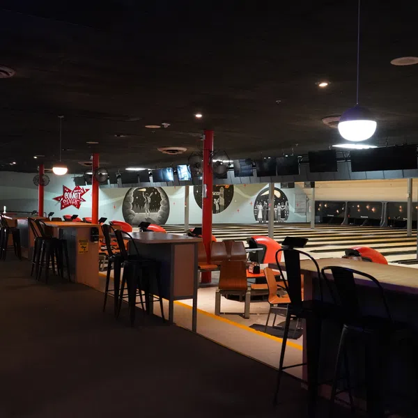 Dimly lit bowling alley with lanes, seating areas, and overhead lights creating a cozy atmosphere.