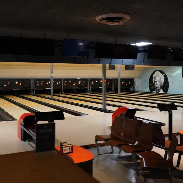Empty bowling alley with multiple lanes, seating area, and mural of a person on the wall under dim lighting