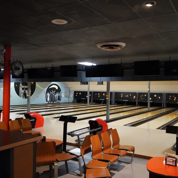 Interior of a bowling alley showing lanes, seating area, and retro-style wall art in dim lighting.
