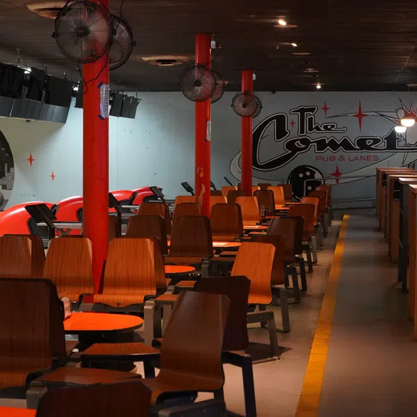 Empty retro-themed bowling alley with wooden chairs, red lanes, and cosmic murals on the walls.