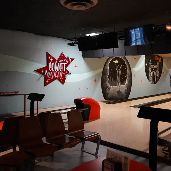 Interior view of a retro bowling alley with wooden seats, lanes, and vintage wall art at Comet Spare.