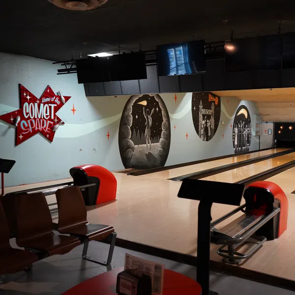 Interior of Comet Spare bowling alley with lanes, seating, and retro-style wall art and signage.