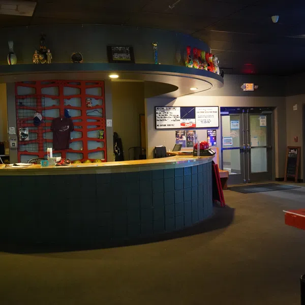 Indoor reception area with curved desk, colorful trophy display, and double glass exit doors under dim lighting