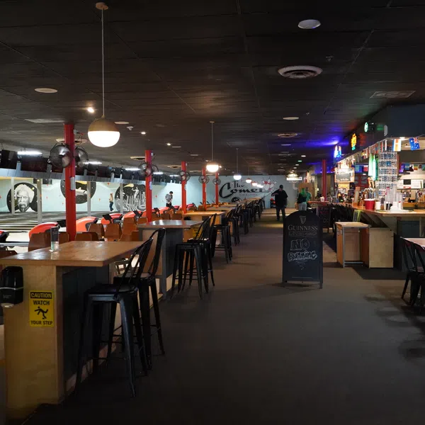 Spacious indoor bowling alley with lanes, seating, bar area, and decorative lighting under dark ceiling.