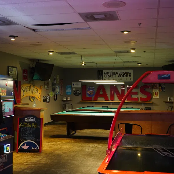 Dimly lit game room with pool tables, arcade machines, and wall signs in a casual entertainment venue.