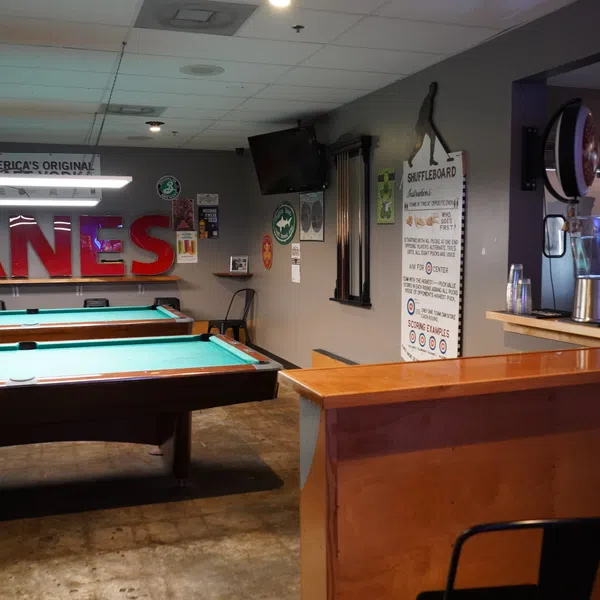 Interior of a game room with pool tables, a bar counter with blenders, and shuffleboard rules on the wall.