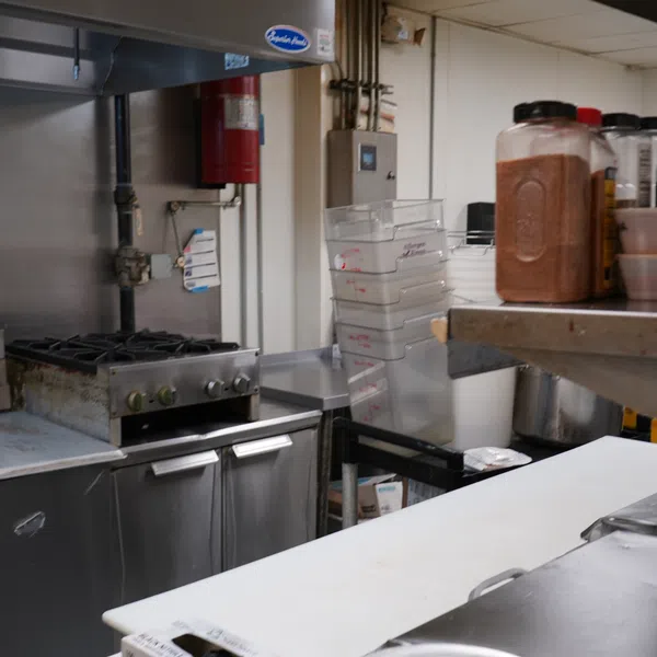 Commercial kitchen with stove, stainless steel counters, storage containers, and cooking spices on shelves.