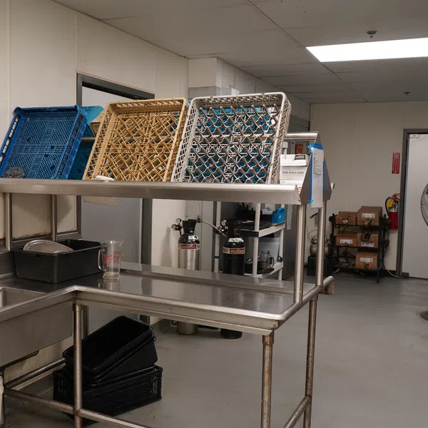 Industrial kitchen dishwashing area with stainless steel sinks, racks drying, and cleaning supplies.