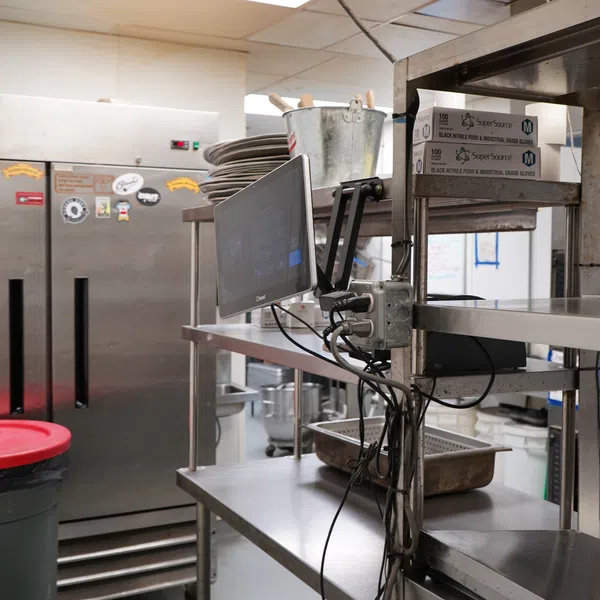 Commercial kitchen area with stainless steel shelves, oven, monitor, and a red-lid trash bin