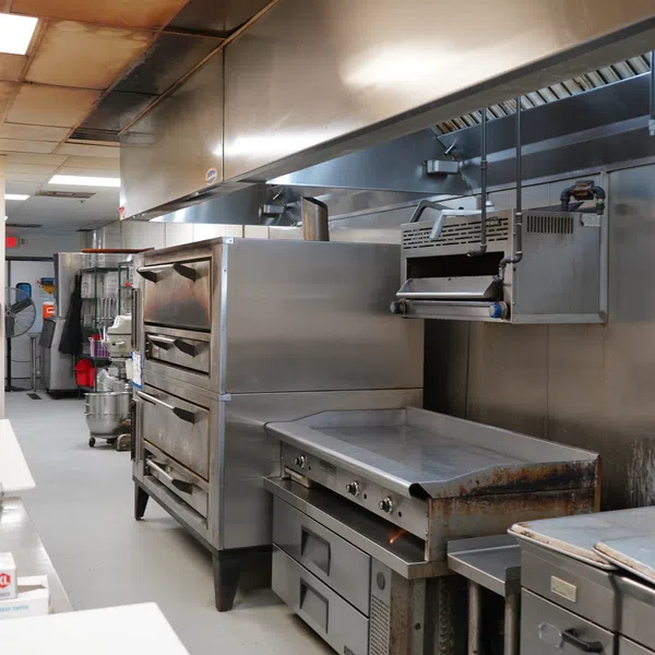 Clean commercial kitchen with stainless steel appliances including ovens, griddle, and prep tables under bright lighting