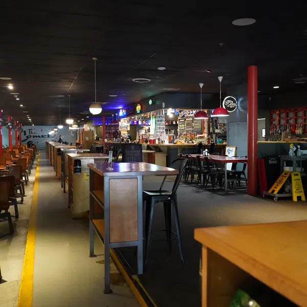 Interior of a bowling alley with seating, tables, bar area, and bowling balls on shelves under warm lighting.