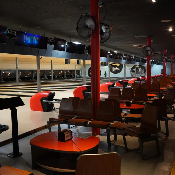 Interior view of an empty bowling alley with multiple lanes, seating areas, and red accents.