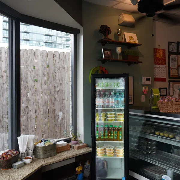 Interior of a cozy shop with a glass refrigerator stocked with beverages and snacks, and a counter with various items.