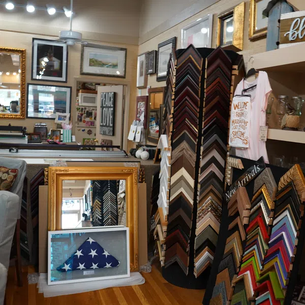 Interior of a frame shop showing various picture frames, mirrors, art prints, and decorative items on shelves.